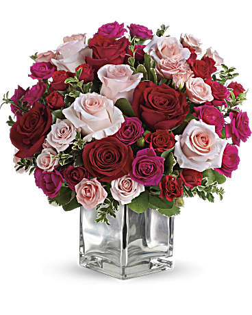 Love Melody bouquet featuring large red and pink roses, smaller spray roses, and fresh greenery in a clear vase.